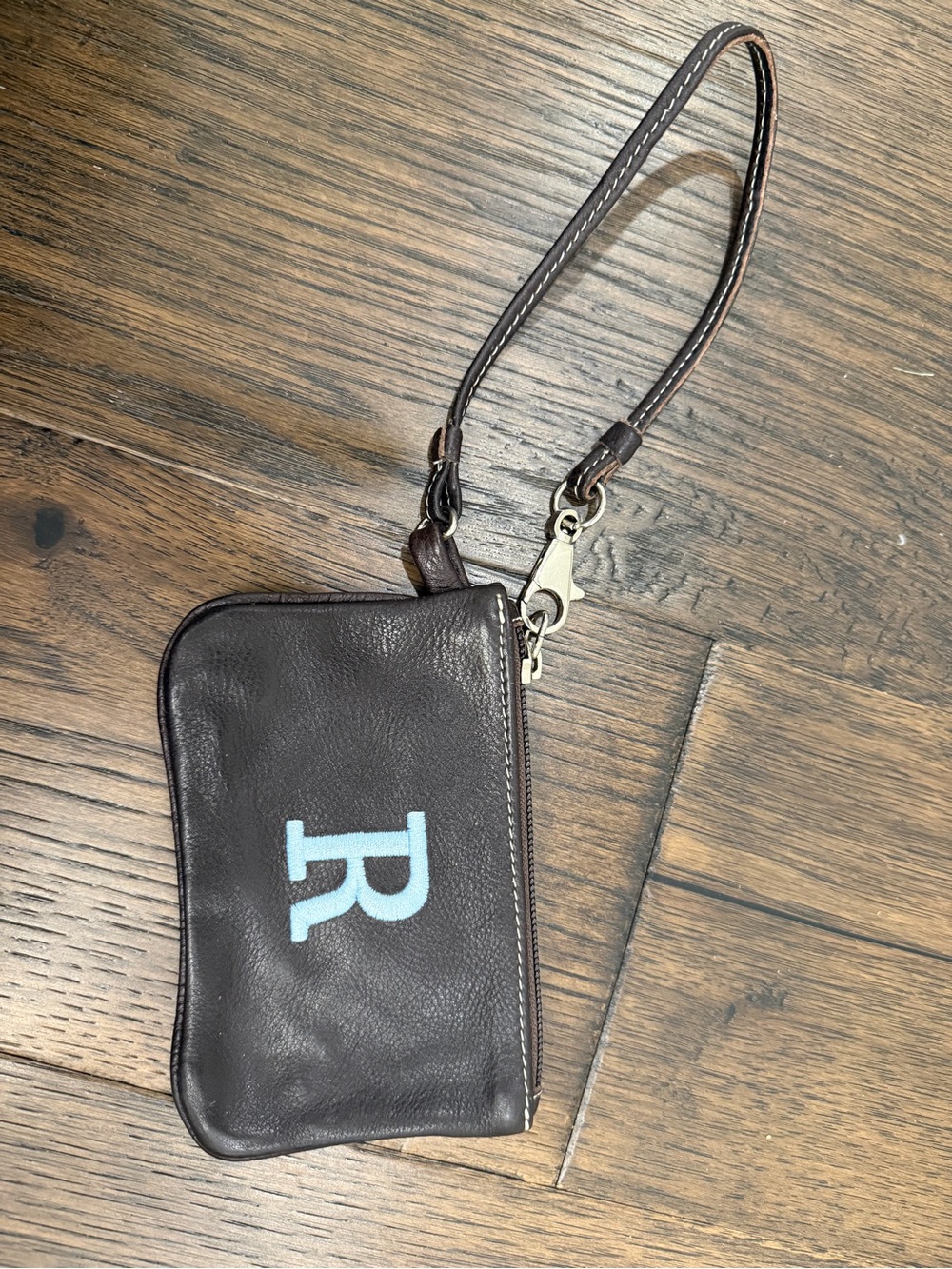 ROOTS chocolate brown leather wristlet with light blue R embroidery.